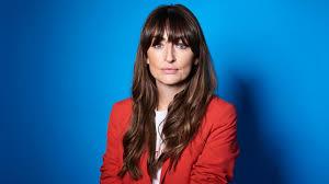 Professional woman in red blazer seated against vibrant blue background, with long brown hair and bangs