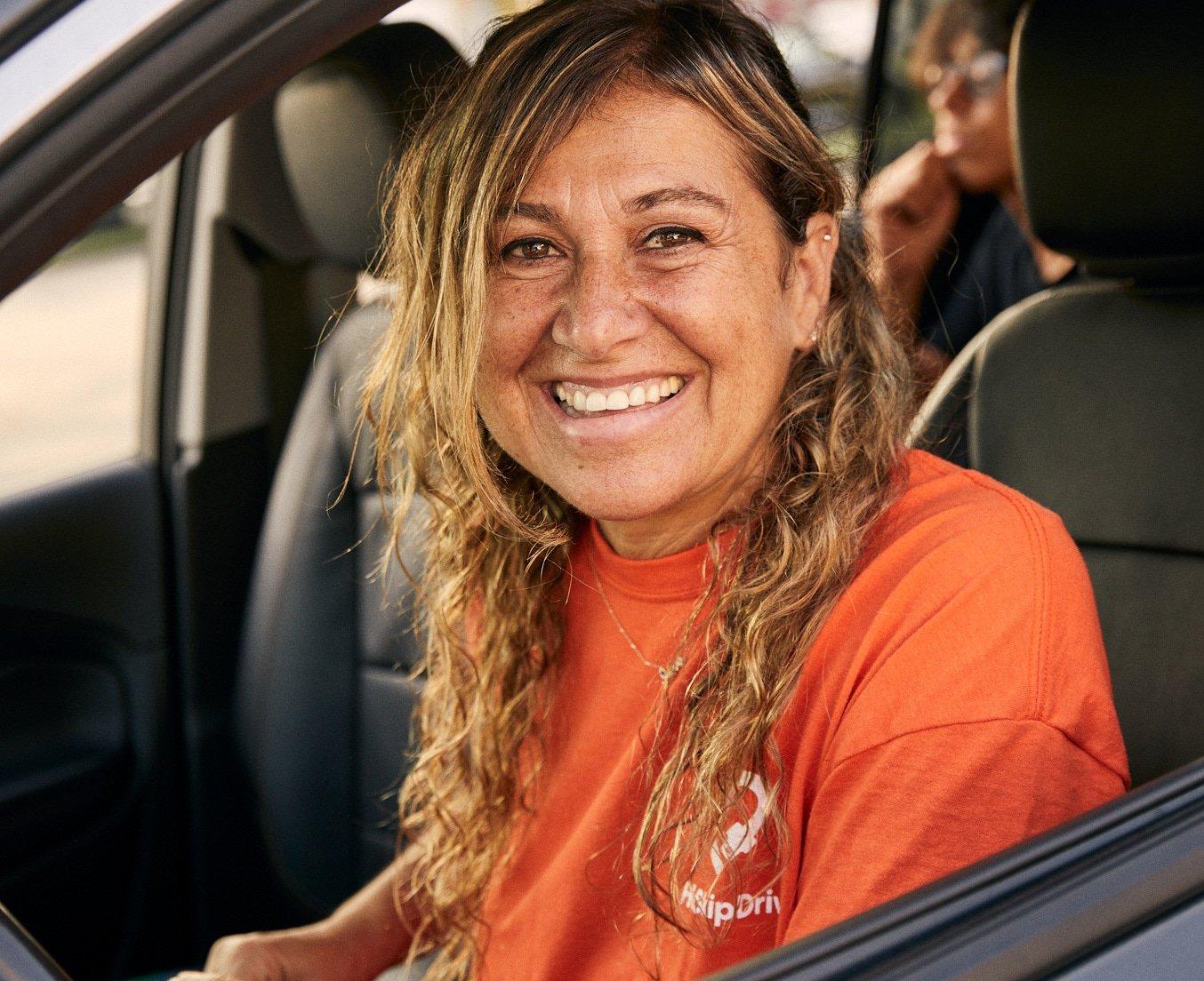 Driver in orange company uniform smiling warmly while sitting in driver's seat of car