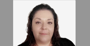 Professional headshot of a person with dark hair wearing black against a gray background, smiling warmly at the camera