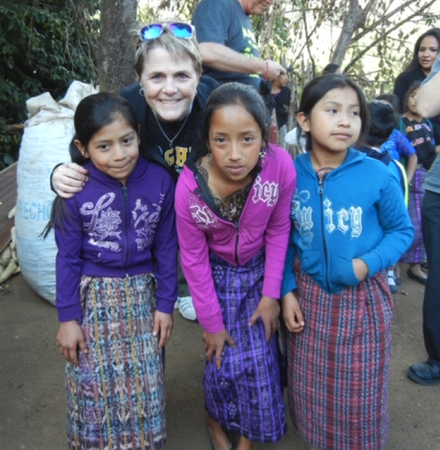 Four people posing together outdoors, wearing colorful traditional Guatemalan skirts and modern sweatshirts in a casual gathering