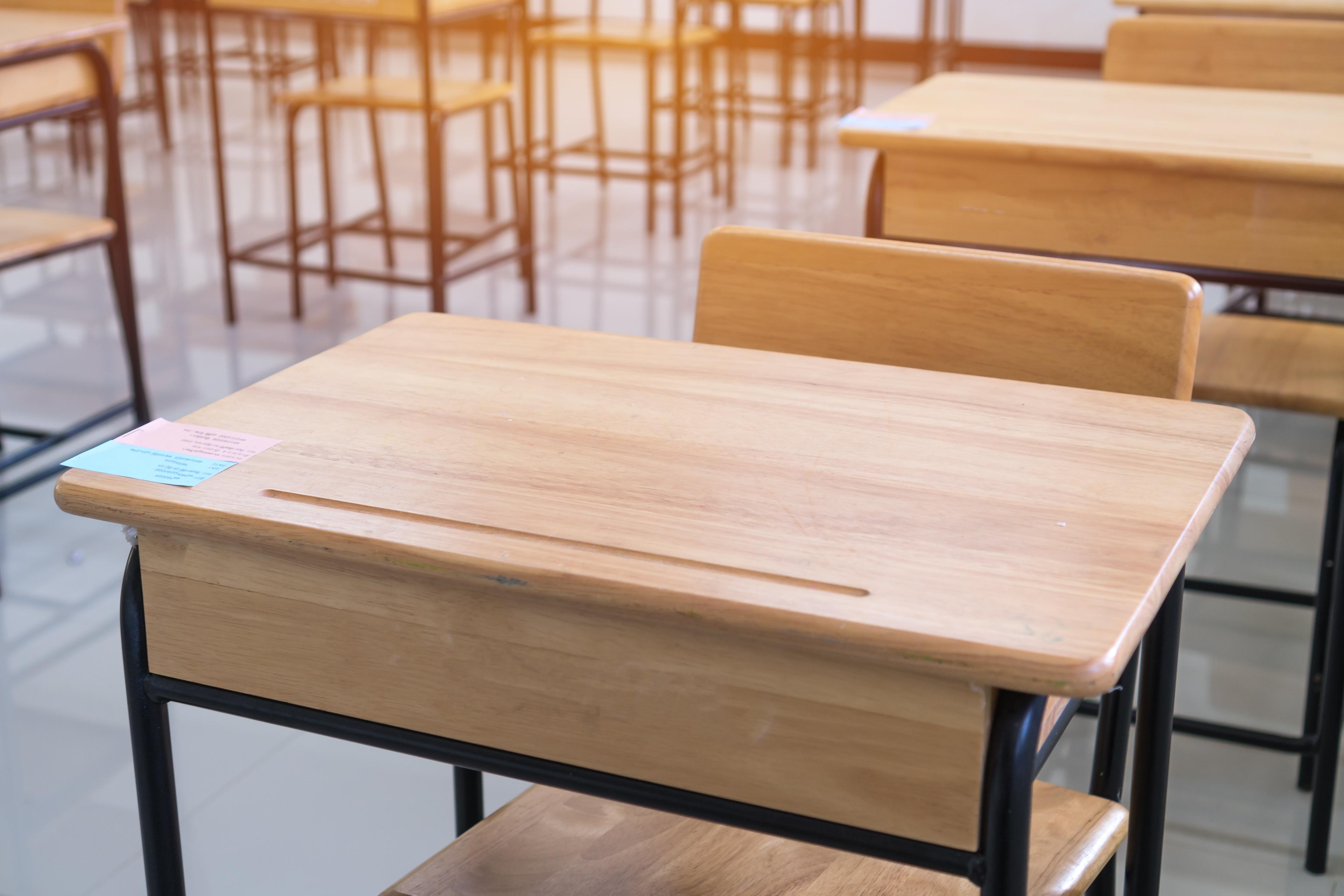 Close-up of an empty wooden school desk with black metal frame in a classroom, with more desks visible in the background