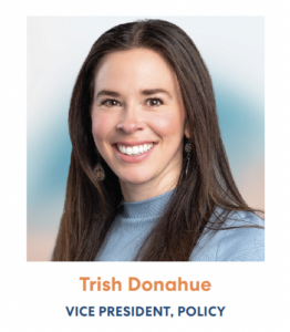 Professional headshot of a person in business attire with a blue background, smiling warmly at the camera