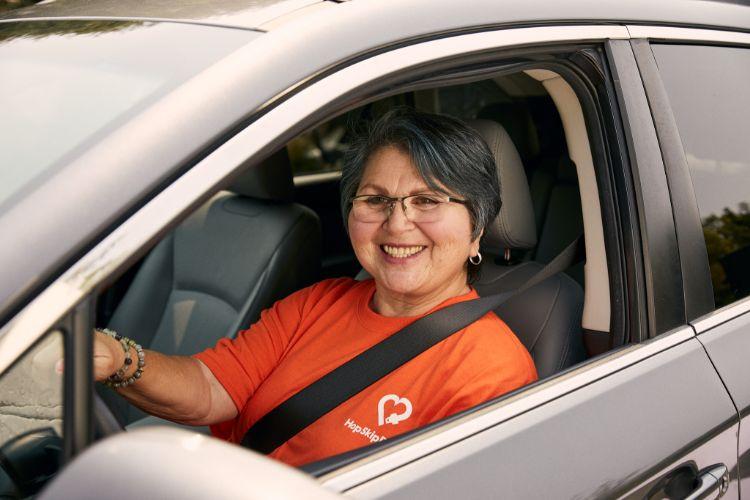 Driver wearing orange company shirt smiling while seated in car with seatbelt on