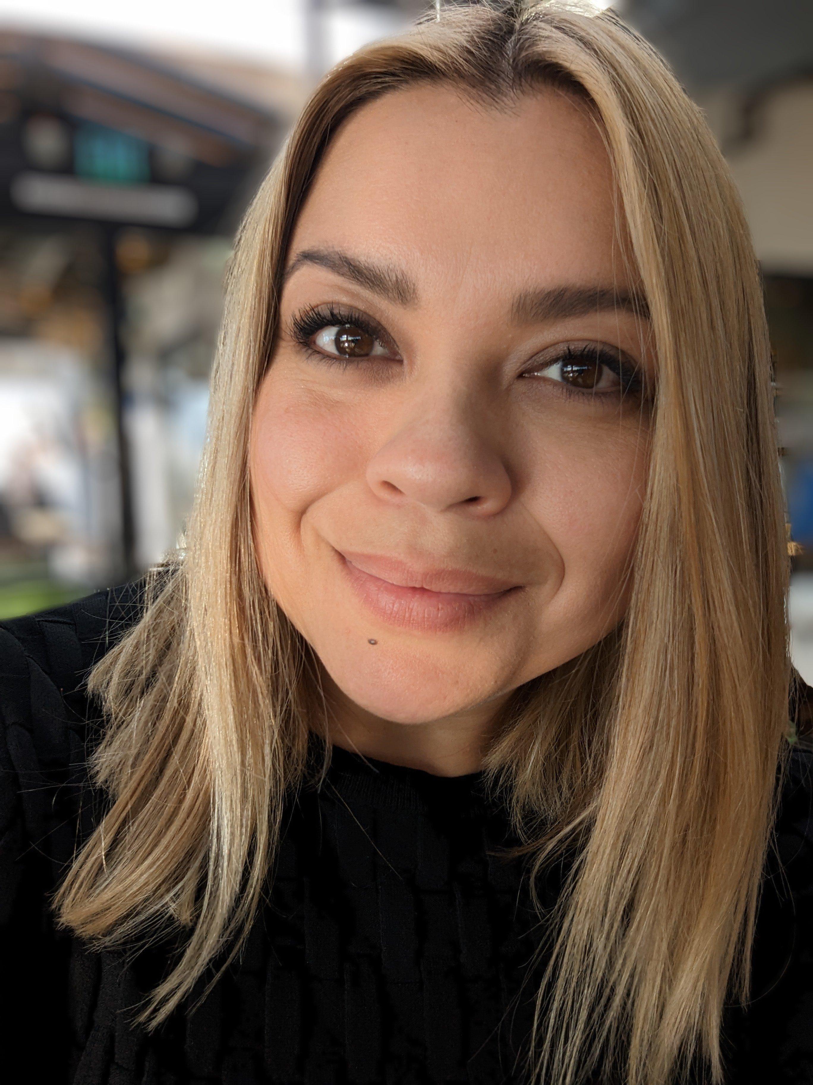 Close-up portrait of a person with blonde hair wearing a black sweater, showing a warm genuine smile