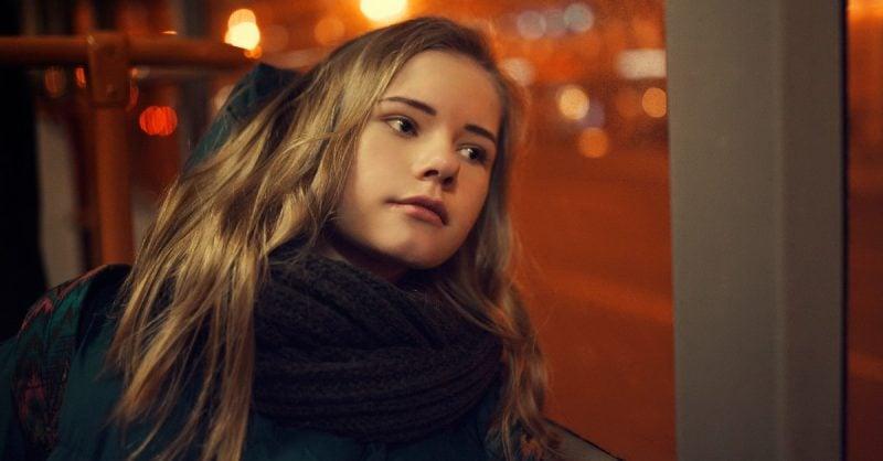 Young woman in knit scarf gazing thoughtfully, warm evening city lights creating bokeh effect in background