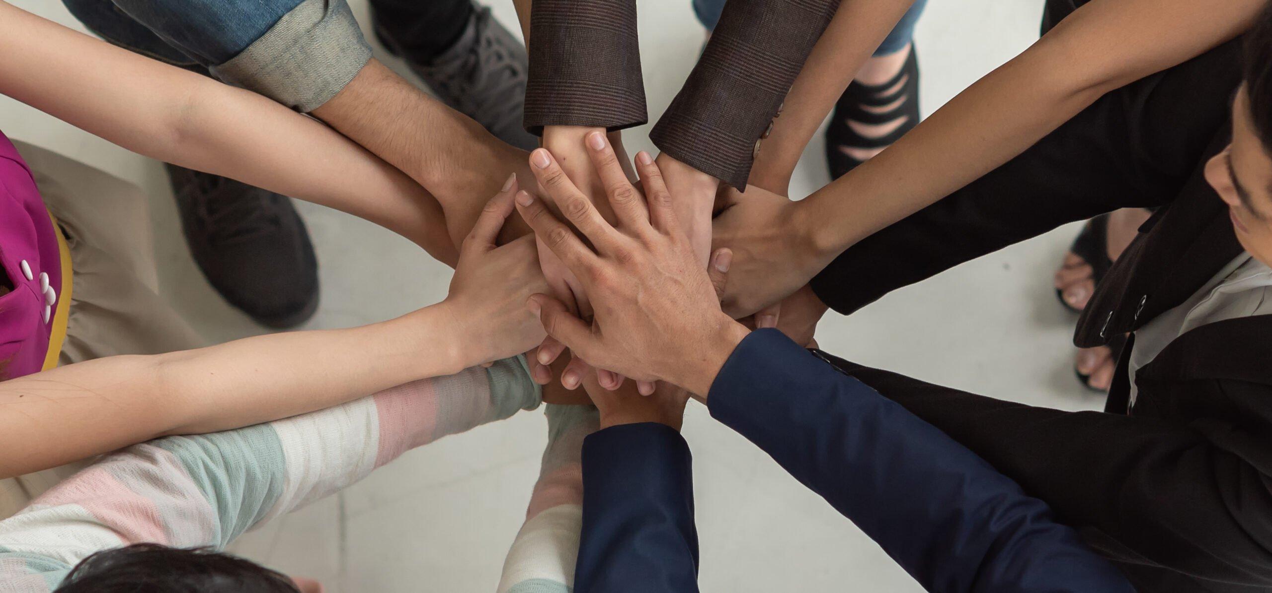 Overhead view of multiple hands stacked together in a circle, symbolizing unity, teamwork, and collaboration