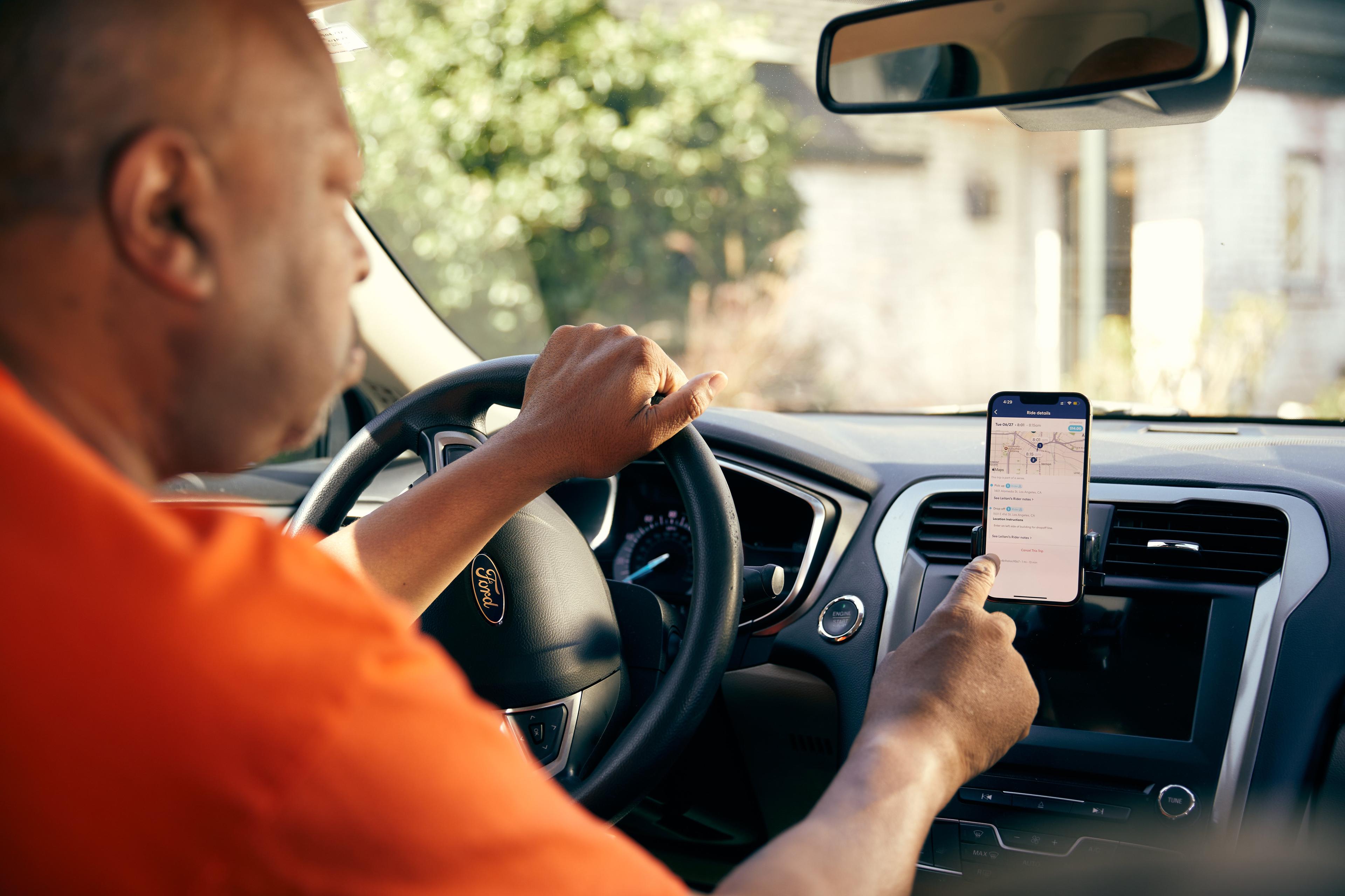 Driver in orange shirt checking navigation app on smartphone while at wheel of Ford vehicle