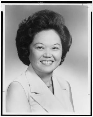 Black and white professional studio portrait of an Asian American woman in business attire with styled hair and warm smile