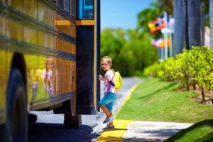 Young student with backpack stepping onto yellow school bus on sunny morning with green landscape in background