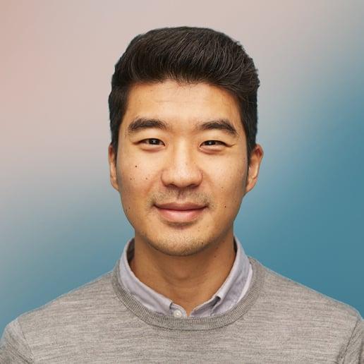 Professional headshot of a young Asian man wearing a grey sweater and collared shirt against a soft gradient background