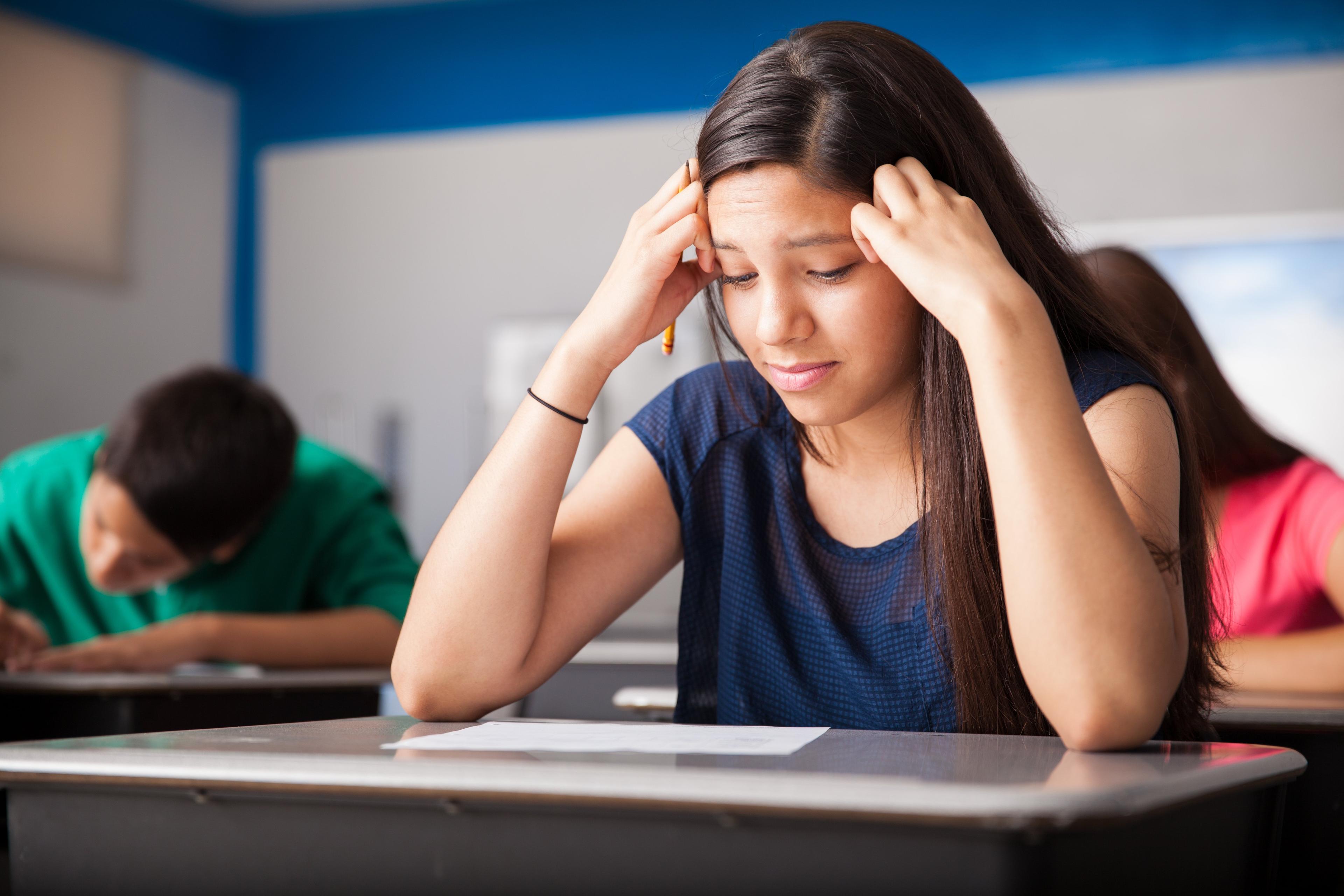 Student with hands on head showing signs of stress while taking test in classroom setting