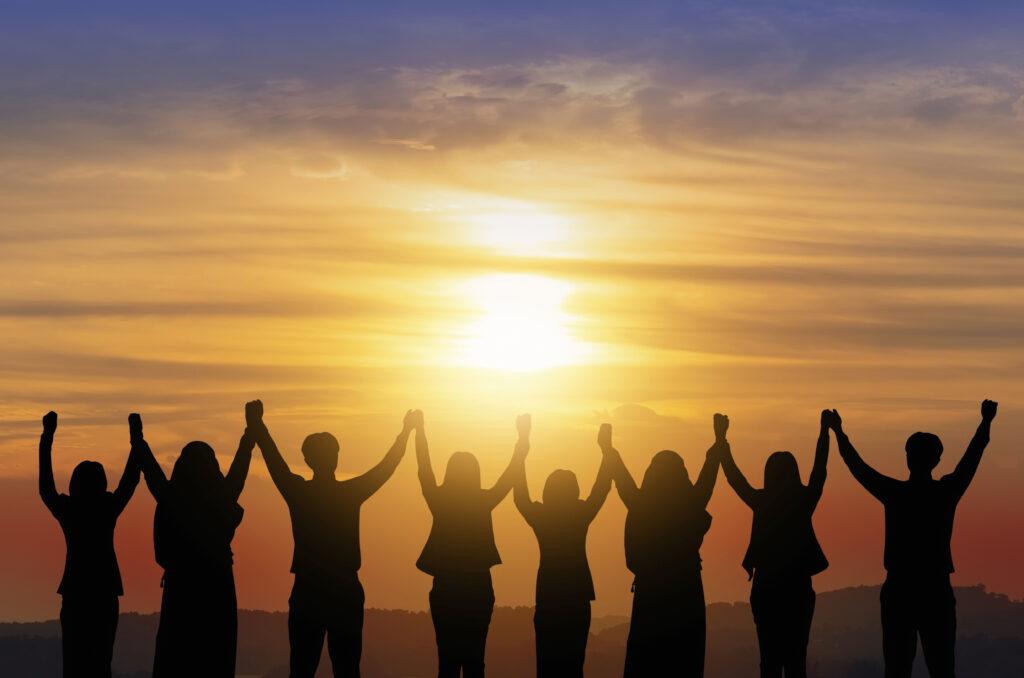 Silhouettes of people holding hands raised in unity against a golden sunset sky