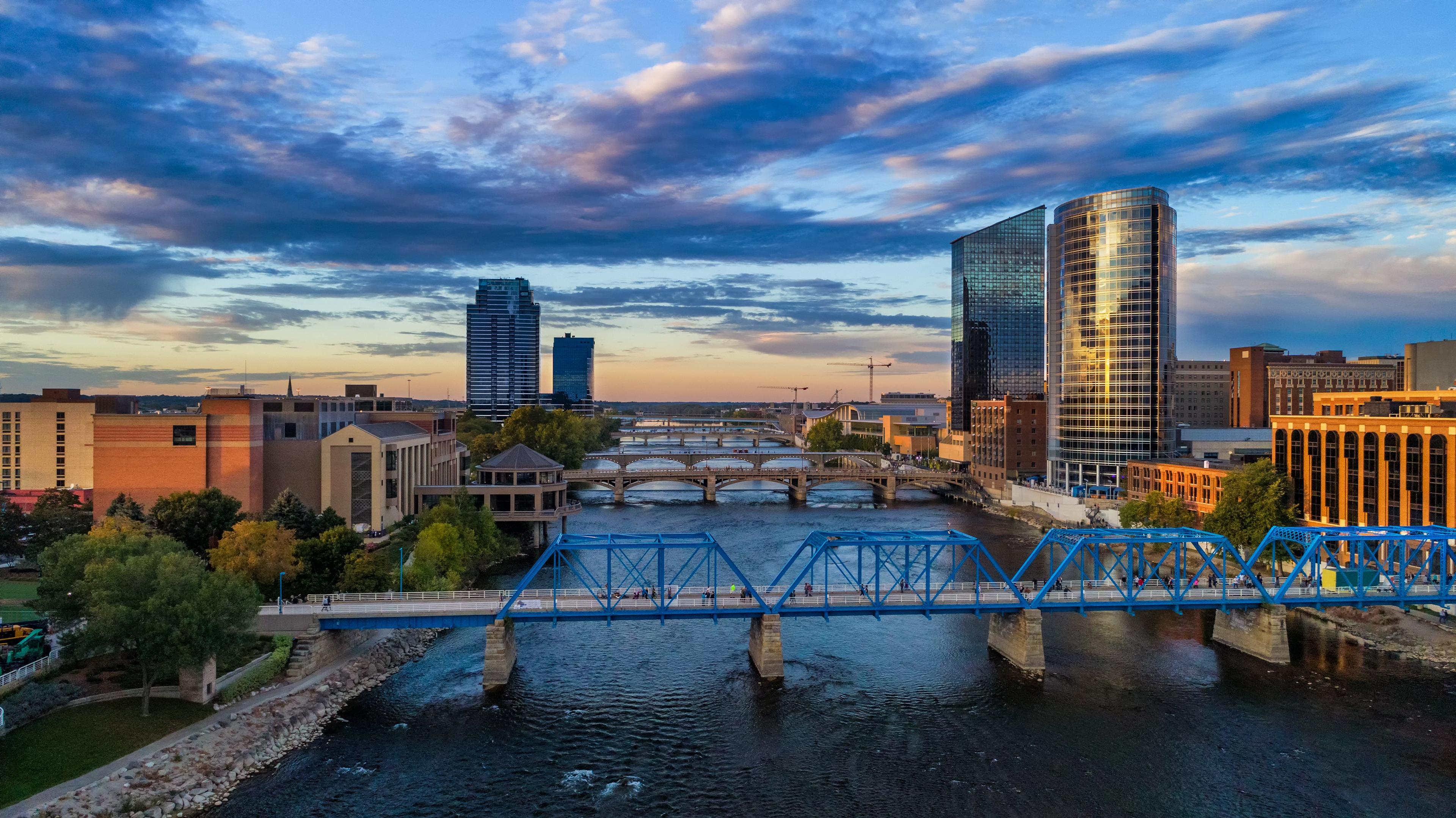 Grand Rapids, Michigan cityscape at sunset featuring the Blue Bridge and Grand River with modern skyscrapers and dramatic clouds