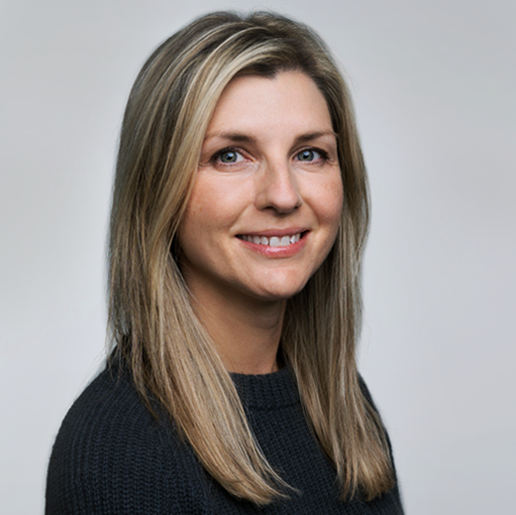 Professional headshot of a woman with long blonde hair wearing a black sweater, smiling warmly against a light gray background
