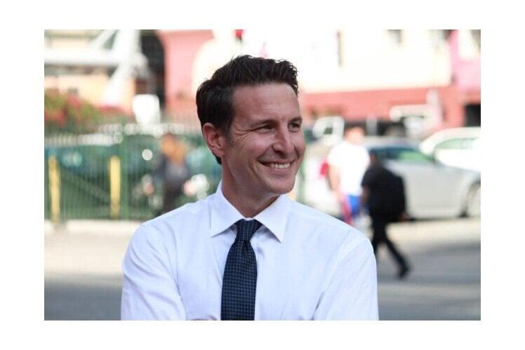 Professional in crisp white dress shirt and navy patterned tie smiling warmly in an outdoor urban setting