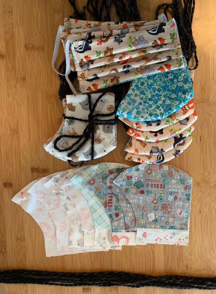 Collection of fabric face masks featuring woodland animals, floral patterns, and children's prints laid out on a wooden surface