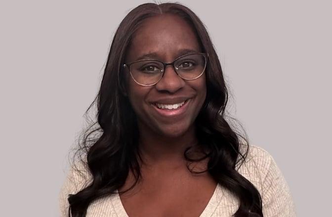 Professional woman wearing glasses and cream sweater smiling warmly at camera against neutral background