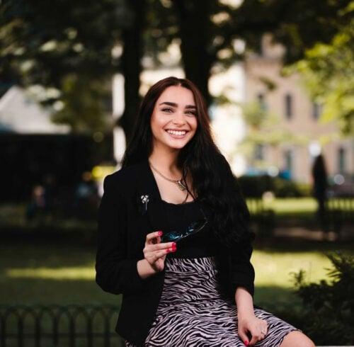 Woman in zebra print dress and black blazer sitting outdoors in a park setting with natural lighting and bokeh effect