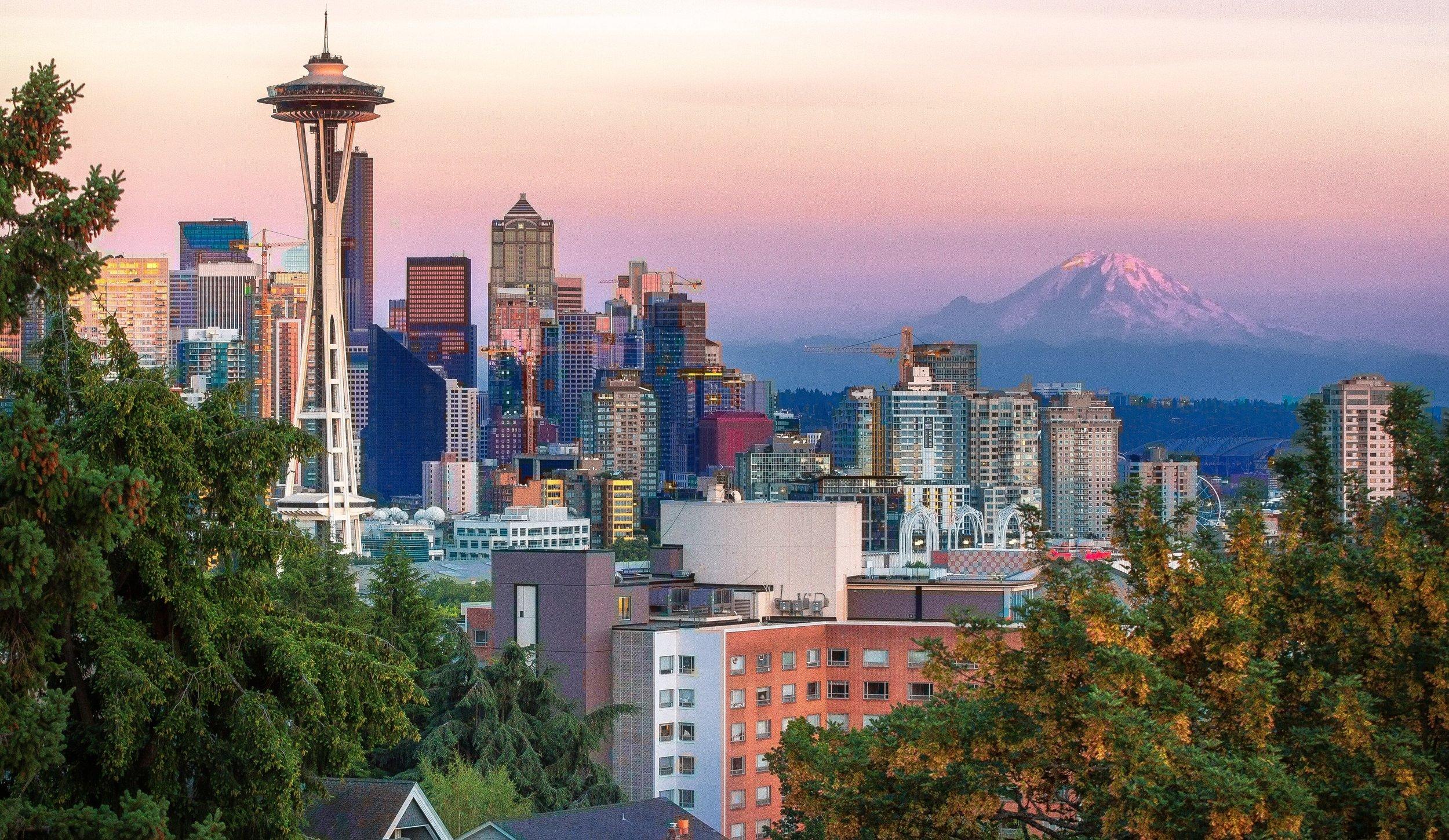 Seattle cityscape featuring Space Needle against pink sunset sky with Mount Rainier in background, framed by autumn trees