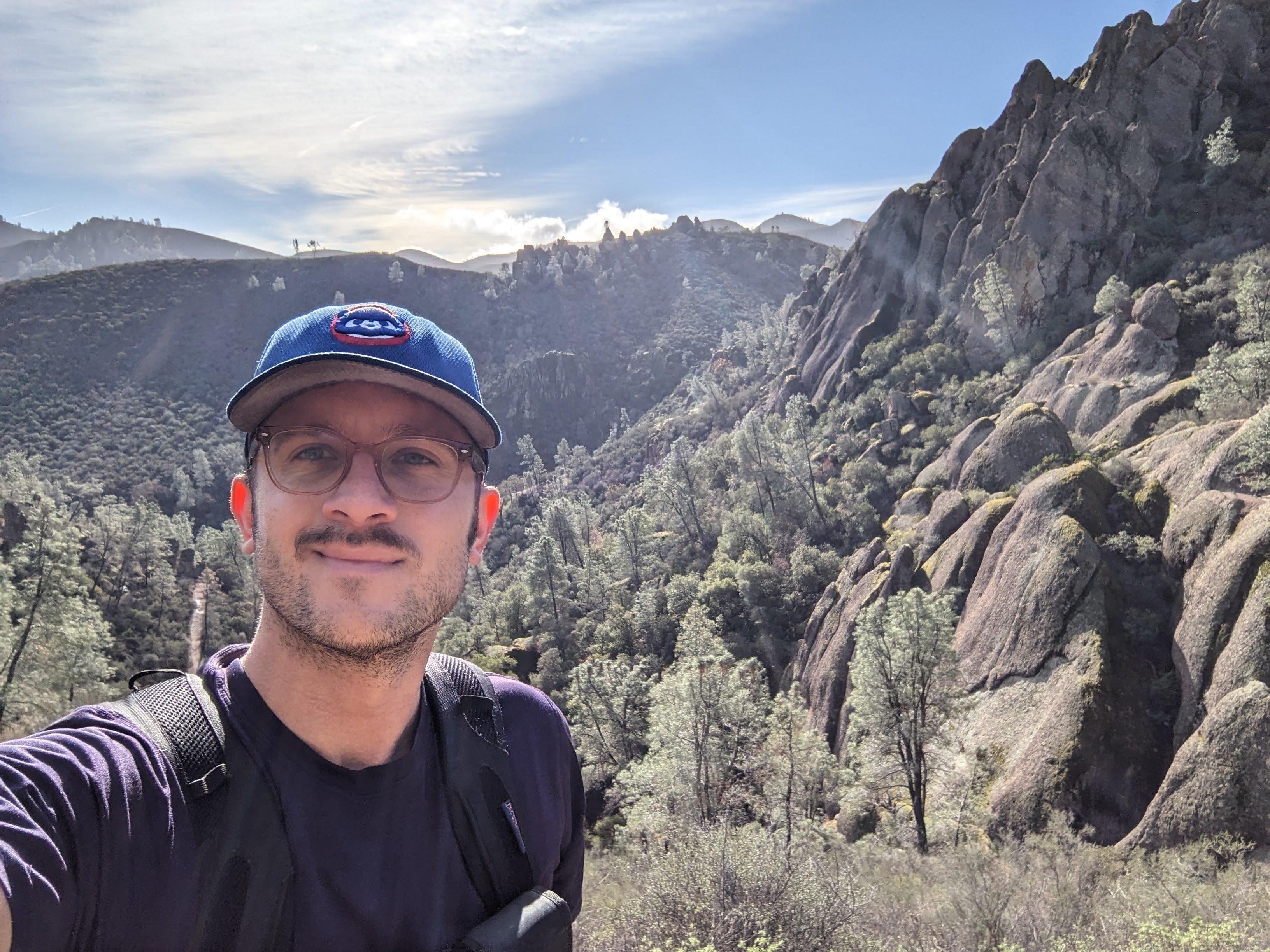 Selfie of hiker wearing Cubs cap with dramatic rock formations of Pinnacles National Park in the background