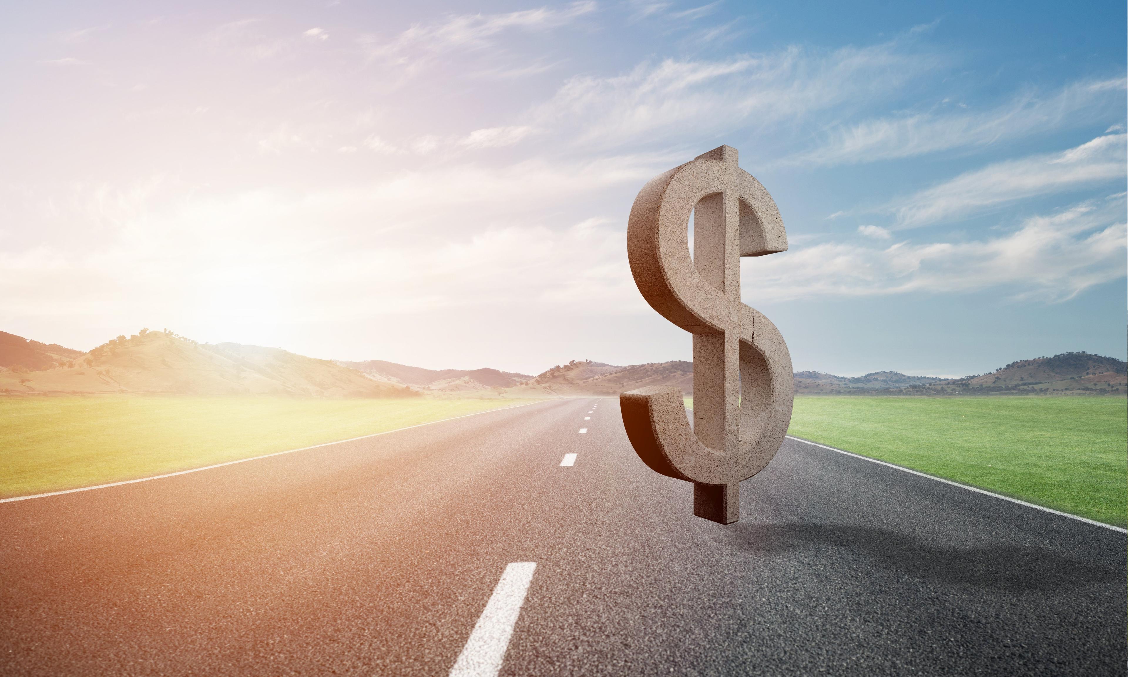 Large 3D dollar sign standing on an empty road stretching toward mountains at sunrise, symbolizing financial journey ahead