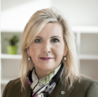 Professional headshot of a woman with blonde hair wearing a dark jacket and patterned scarf, photographed against a light interior background
