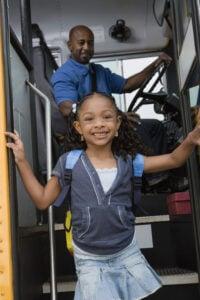 Young student smiling while boarding yellow school bus with driver visible in background