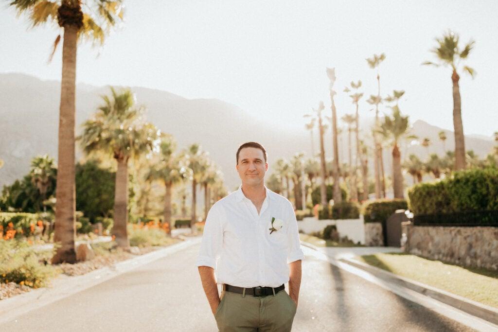 Person in white shirt and khakis standing on palm tree-lined path during golden hour with mountains in background