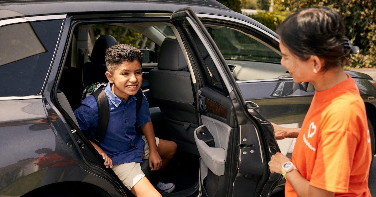 Young student in back seat of car smiling at driver in orange service uniform