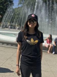 Person in black Adidas t-shirt and baseball cap standing in front of a water fountain on a sunny day