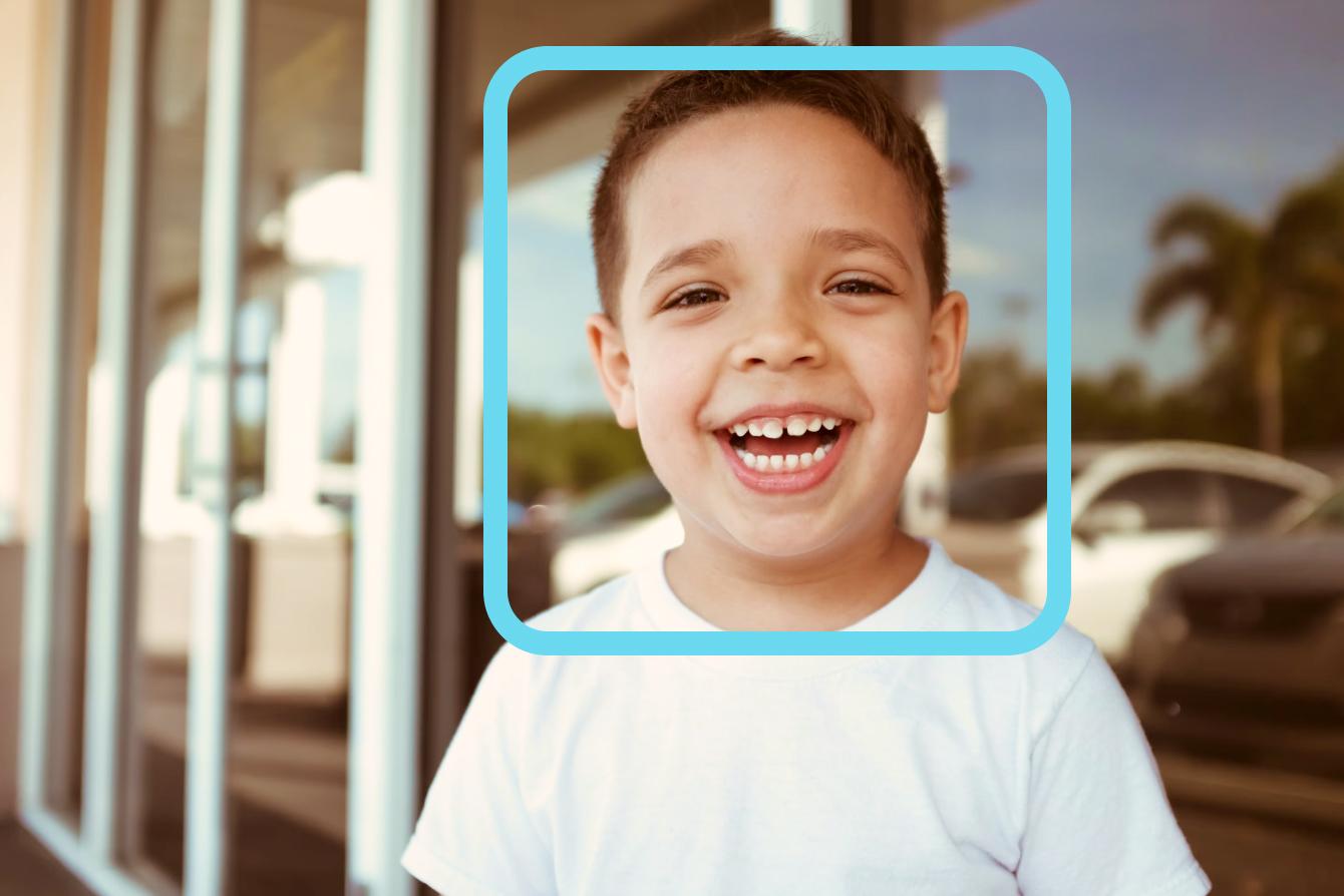 A young child wearing a white t-shirt smiles brightly at the camera, showing genuine joy