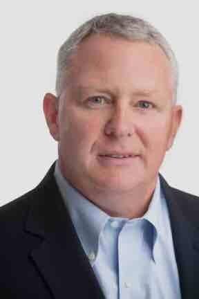 Professional headshot of a middle-aged person in business attire against a light gray background