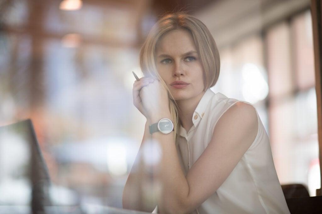 Young professional woman in white sleeveless blouse sitting thoughtfully in office setting wearing minimalist watch