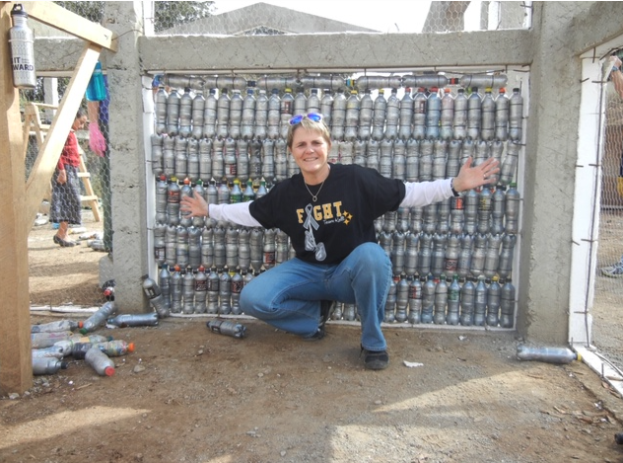Person posing enthusiastically in front of a wall made of recycled plastic bottles arranged in neat vertical rows