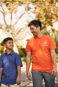 Mentor in orange charity shirt and young boy in blue polo sharing a genuine moment of connection outdoors during autumn