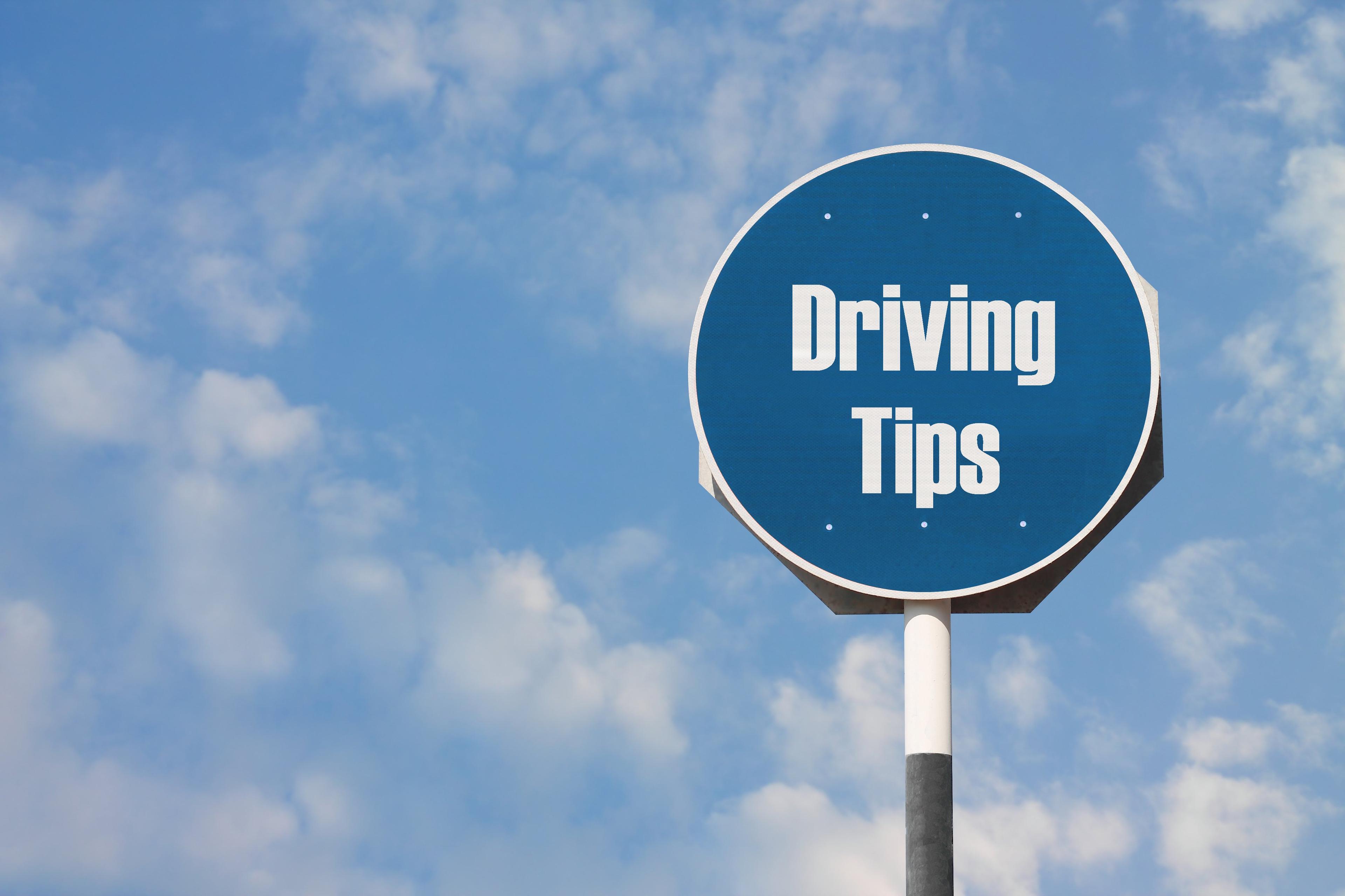 A blue circular road sign reading 'Driving Tips' against a cloudy blue sky background