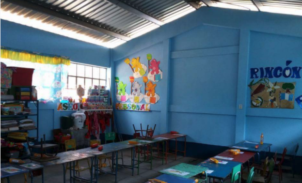 Empty classroom with blue walls, decorated with colorful artwork and educational materials, featuring student desks and learning spaces