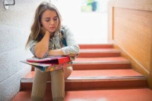 Student sitting on interior staircase with books and notebooks, appearing thoughtful while studying