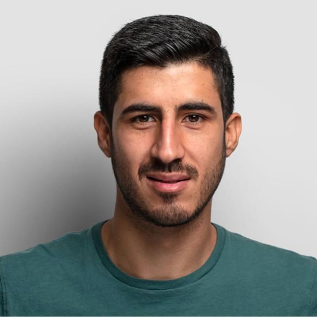 Professional portrait of a young man wearing a green t-shirt against a white background, with a warm smile