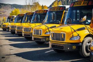Row of parked yellow school buses lined up diagonally with mountains in the background