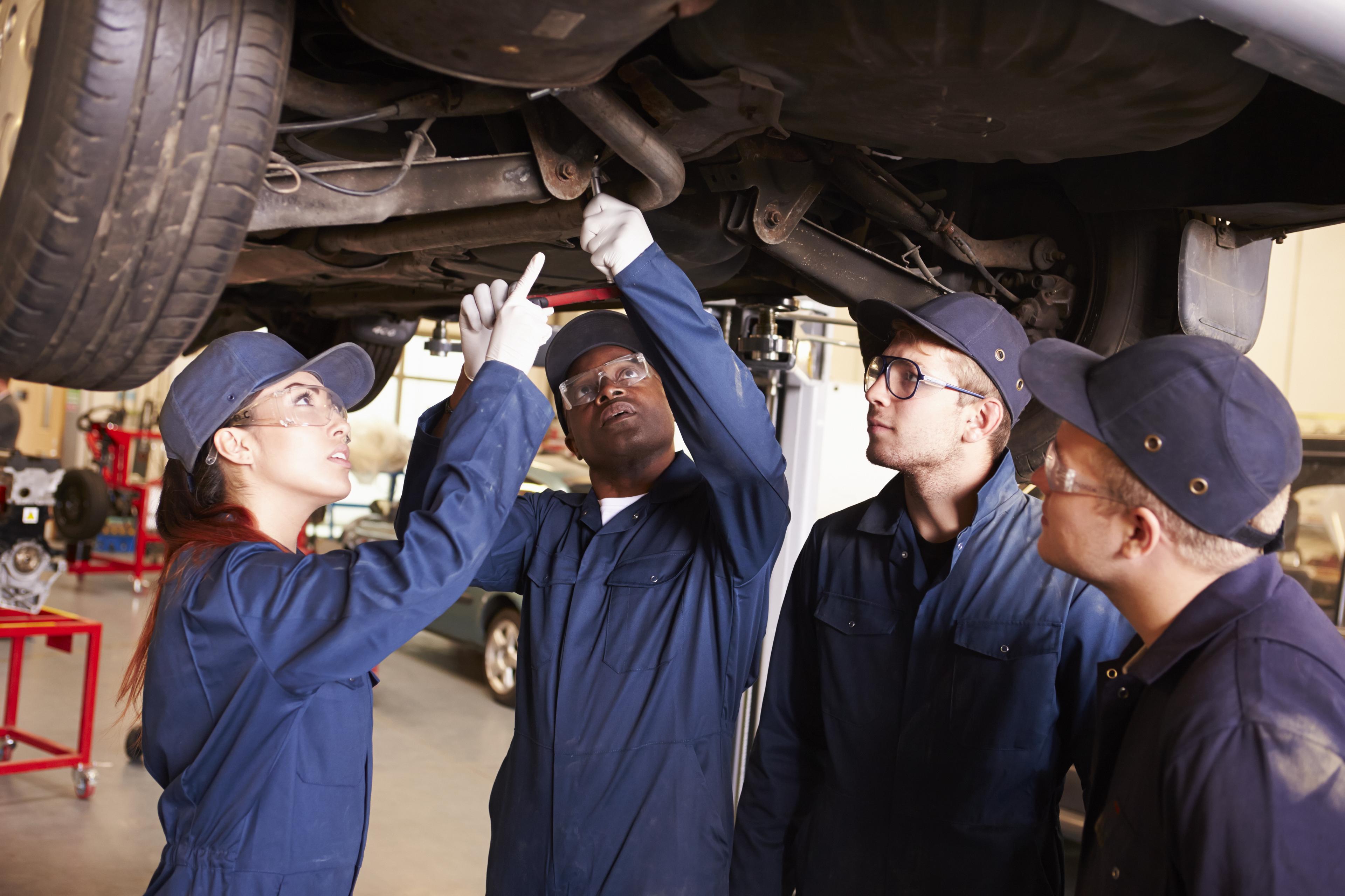 Group of auto mechanics in blue uniforms examining the undercarriage of a vehicle during a training or inspection session