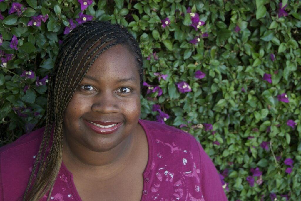Portrait of a person smiling warmly at the camera against a background of purple flowers and green foliage