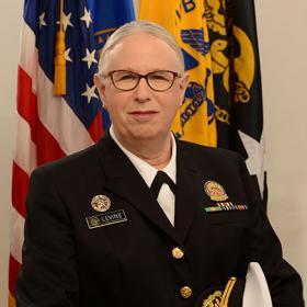Official portrait of a uniformed public health service officer in front of American and service flags