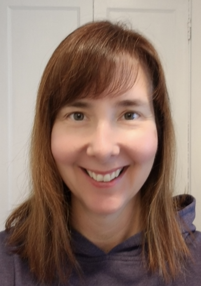 Close-up portrait of a person with brown hair wearing a navy hoodie, smiling warmly at the camera