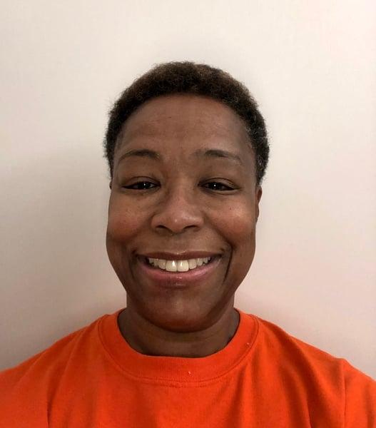 Professional headshot of person wearing bright orange t-shirt, showing warm genuine smile against neutral background